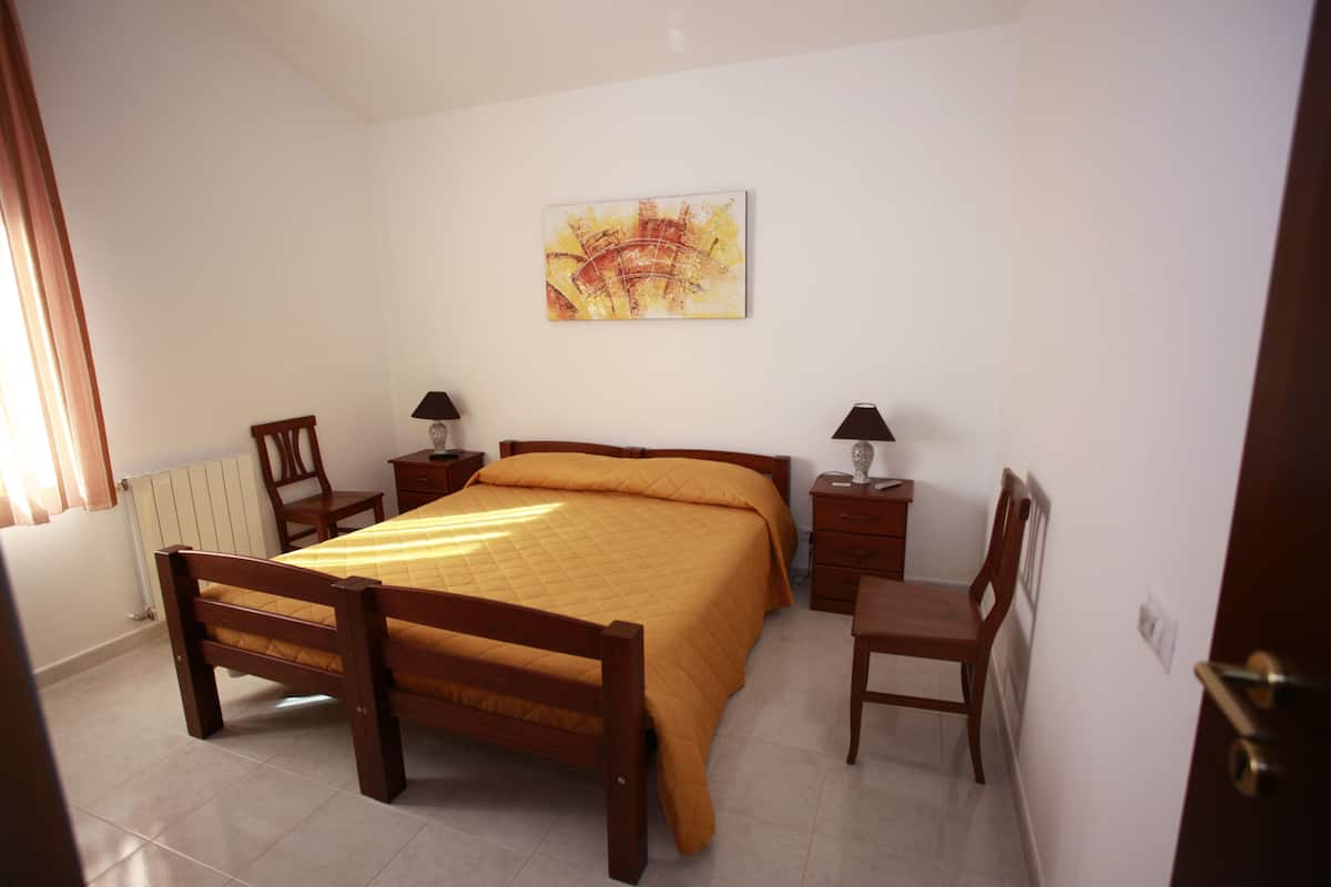 A bedroom with a wooden bed, two bedside tables with lamps, a chair, and a painting on the wall.