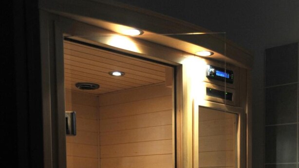 A sauna with a wooden interior, a glass door, and a control panel on the right side. - Sicily Bike (Serradifalco)