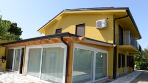 A yellow two-story house with a covered patio, large sliding glass doors, and a balcony. - Sicily Bike (Serradifalco)
