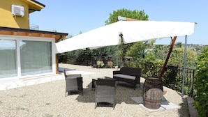 An outdoor patio with wicker furniture, a white umbrella, and a rustic barrel. - Sicily Bike (Serradifalco)