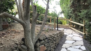 A stone pathway leading through a garden with a wooden fence and a tree. - Sicily Bike (Serradifalco)