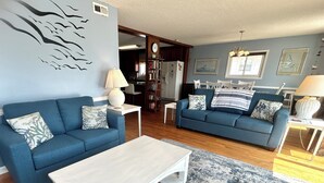 A living room with two blue sofas, a white coffee table, and a patterned rug. - Pier View: Cozy Second Row Beach Cottage with Sunroom, Great Views and Easy Beach Access (Brunswick)