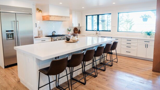 A modern kitchen with a large island, bar stools, stainless steel appliances, and ample natural light from large windows.