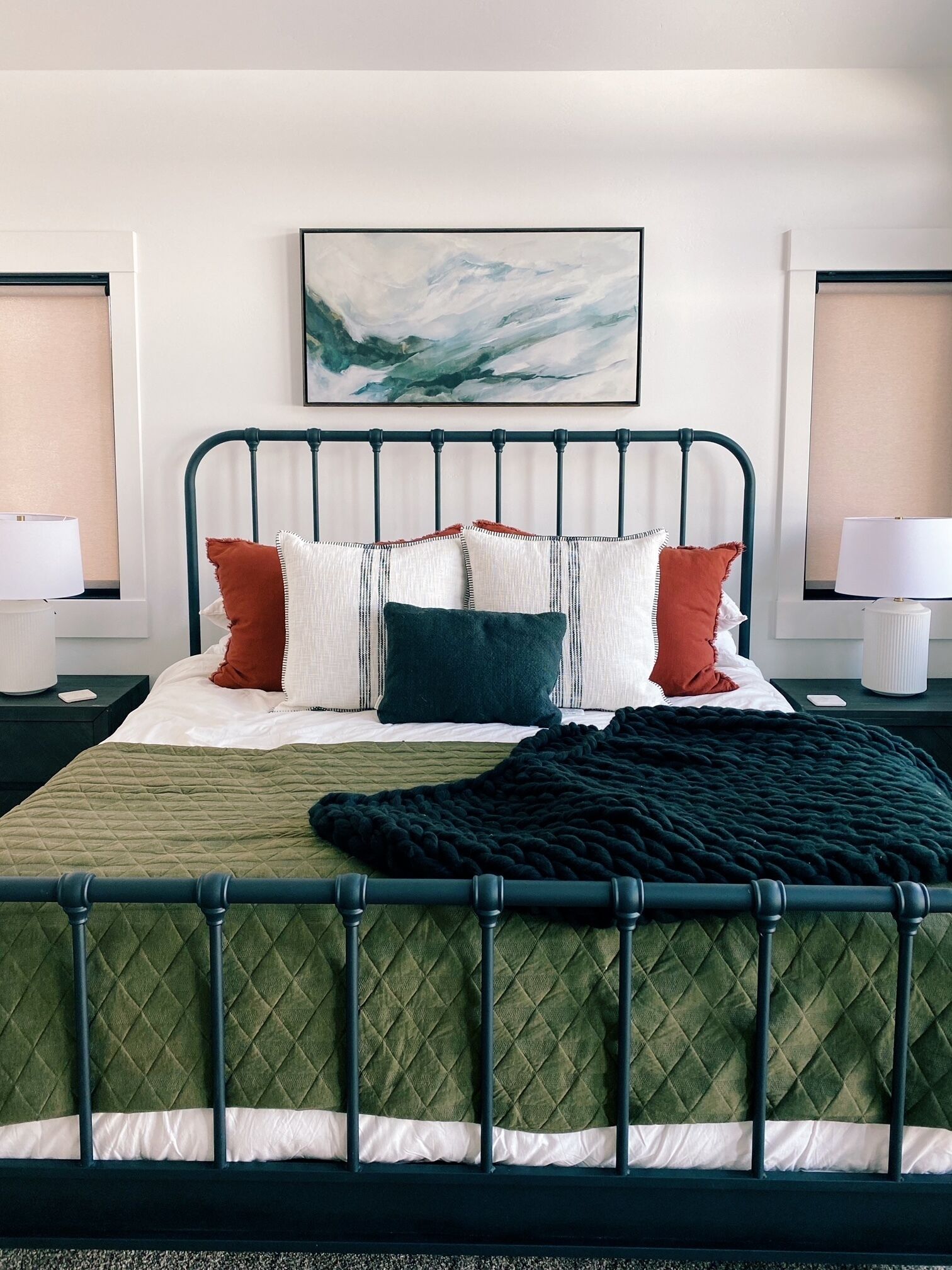 Un letto rifatto con cura, con una coperta verde, numerosi cuscini e una coperta da letto nera.