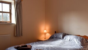Ein Schlafzimmer mit einem Bett, einem Nachttisch, einer Lampe und einem Fenster mit Vorhängen.