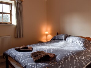 A bedroom with a bed, a nightstand, a lamp, and a window with curtains.