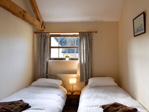 Una habitación con dos camas, una ventana con cortinas, un radiador y un cuadro en la pared.