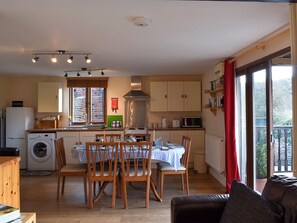 A compact kitchen with a washing machine, a dining table with chairs, and a view through a large window.