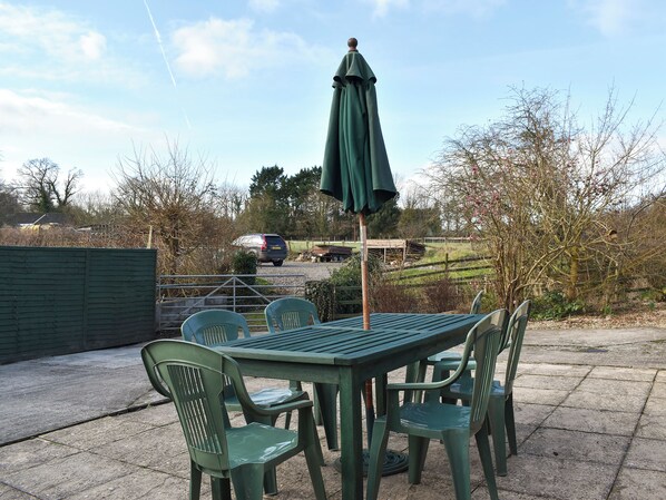 An outdoor patio with a table and chairs, a green umbrella, and a car in the background.