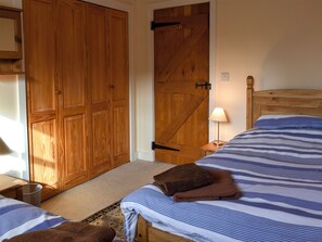 A bedroom with a wooden wardrobe, a bed with striped bedding, a bedside lamp, and a small rug.
