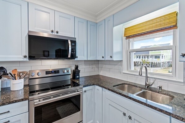 A modern kitchen with white cabinets, stainless steel appliances, granite countertops, and a window with a view of a house.