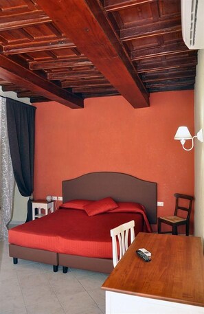 Un dormitorio con techo de madera, una cama con colcha roja, una mesita de noche, una silla y una lámpara.