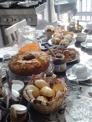 Una mesa de desayuno con diversos pasteles, pan y una jarra de jugo de naranja.