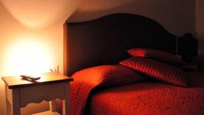 Un dormitorio con cama, almohadas y una mesita de noche con control remoto.
