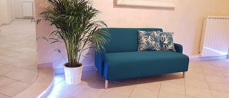 A teal sofa with a leaf-patterned pillow, a potted plant, and a framed picture on the wall.