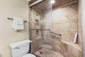 A glass-enclosed shower with a handrail, a white toilet, and a towel rack.