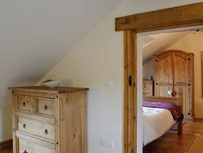 Un dormitorio con un aparador de madera, una cama con manta morada y un armario de madera.