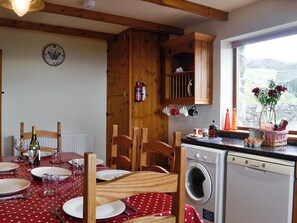 Une cuisine avec des meubles en bois, un lave-linge et un coin repas agrémenté d’une nappe à pois rouges.