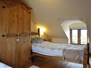 Une chambre à coucher avec un lit en bois, une armoire, une table de chevet et une fenêtre donnant sur un paysage verdoyant.