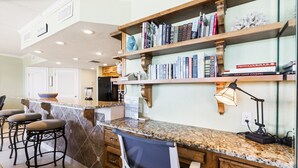 Une cuisine dotée de plans de travail en granit, de tabourets de bar, d’une bibliothèque intégrée et d’une machine à café.