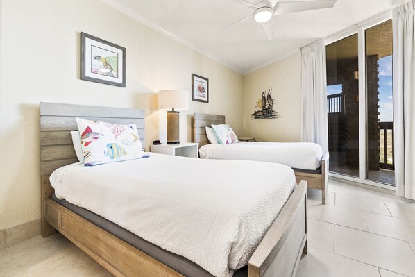 A bedroom with two beds, a ceiling fan, and a view of the outside through a sliding glass door.