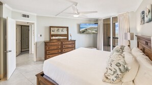 Une chambre dotée d’un grand lit, d’un ventilateur de plafond, d’une commode, d’un téléviseur et d’un balcon agrémenté de rideaux.
