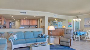 Ein geräumiges Wohnzimmer mit einem blauen Sofa, einem Glastisch und einem Essbereich mit gestreiftem Tischläufer.
