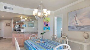Ein Essbereich mit gestreifter Tischdecke, weißen Stühlen und einer Chandelier. An der Wand hängt ein Gemälde eines Segelboots.