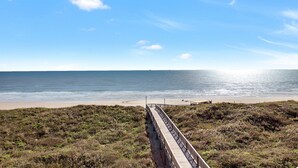 Ein hölzerner Steg führt zu einem Strand bei blauem Himmel.