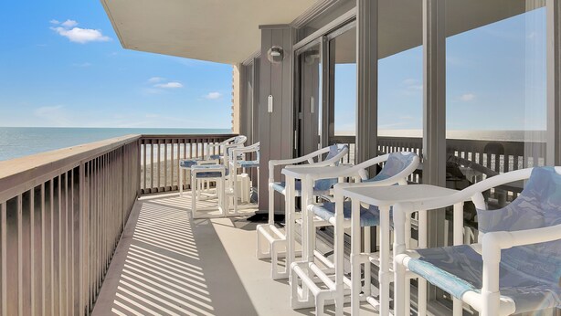 Ein Balkon mit weißen Stühlen und Tischen mit Blick auf einen Strand.