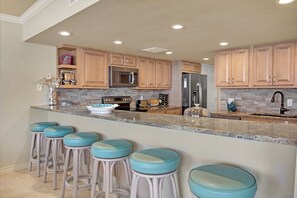 Cocina con armarios de madera, encimera de granito y cuatro taburetes de bar.