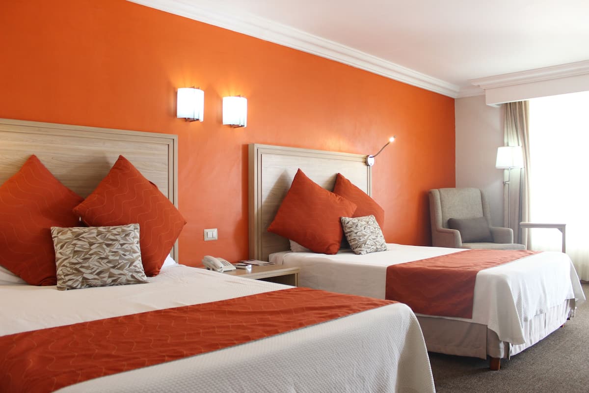 A hotel room with two beds, orange walls, and a chair.