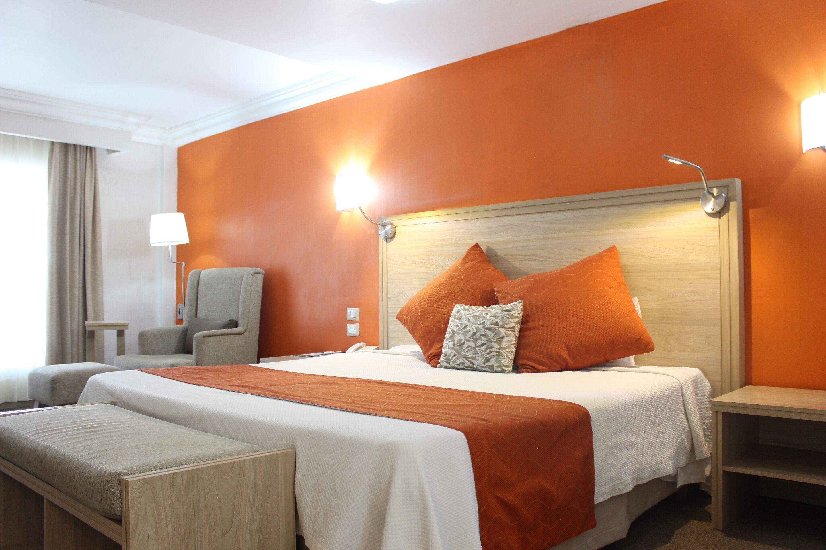 A hotel room with a large bed, a chair, a nightstand, and a lamp.
