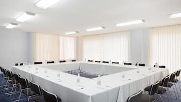 Un salón de conferencias con una larga mesa, sillas y botellas de agua.