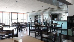 A restaurant with multiple tables and chairs, a bar area, and a kitchen visible in the background.