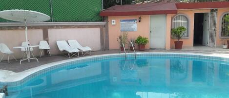 Una piscina con sillones de descanso y un pequeño edificio de techo rojo.
