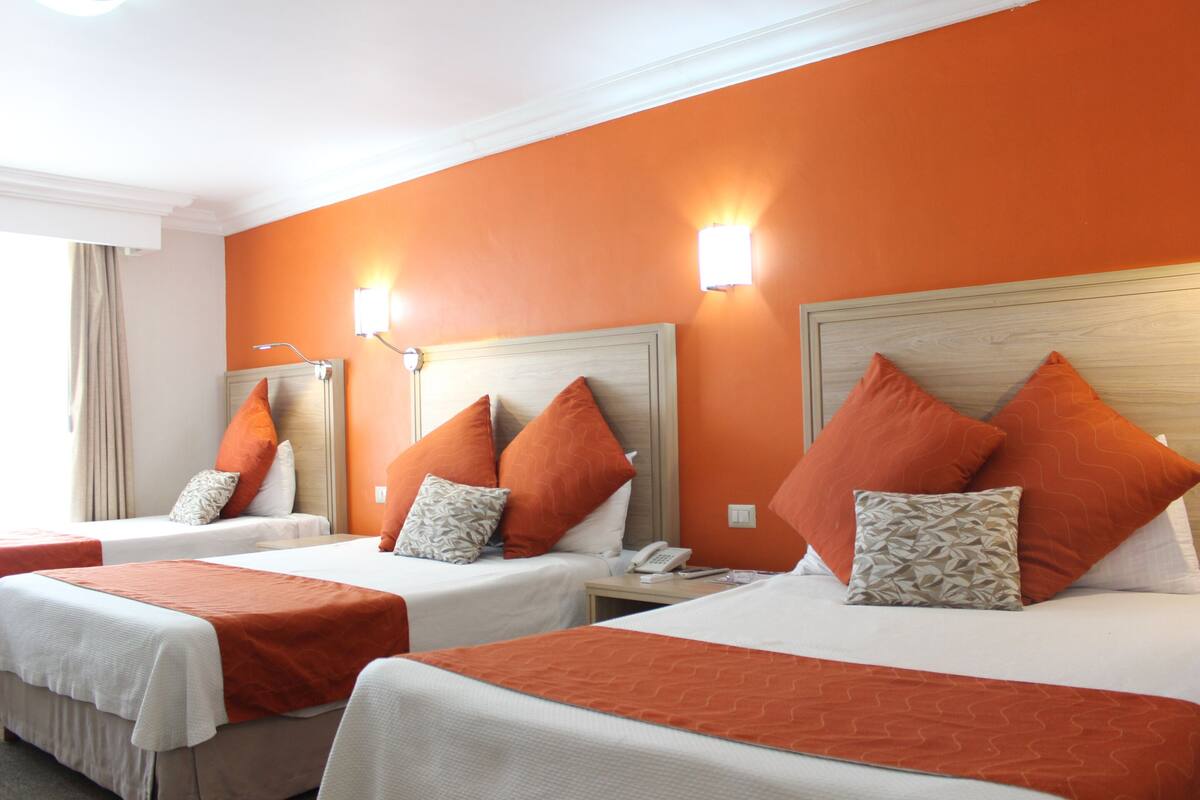 A hotel room with two beds, orange walls, and a wooden headboard.