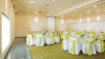 A conference room with multiple tables and chairs, each covered with white tablecloths and green sashes, arranged in rows.