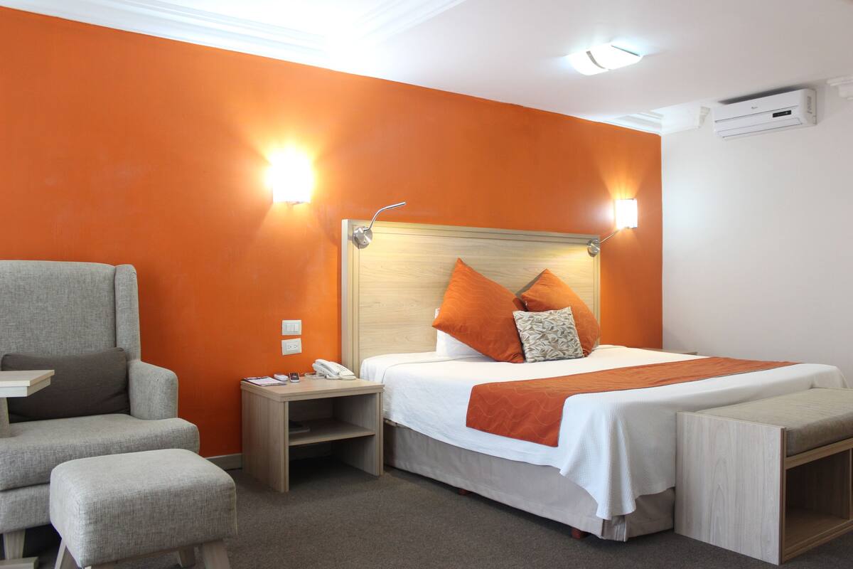 A hotel room with a bed, a chair, a bedside table, and a nightstand.
