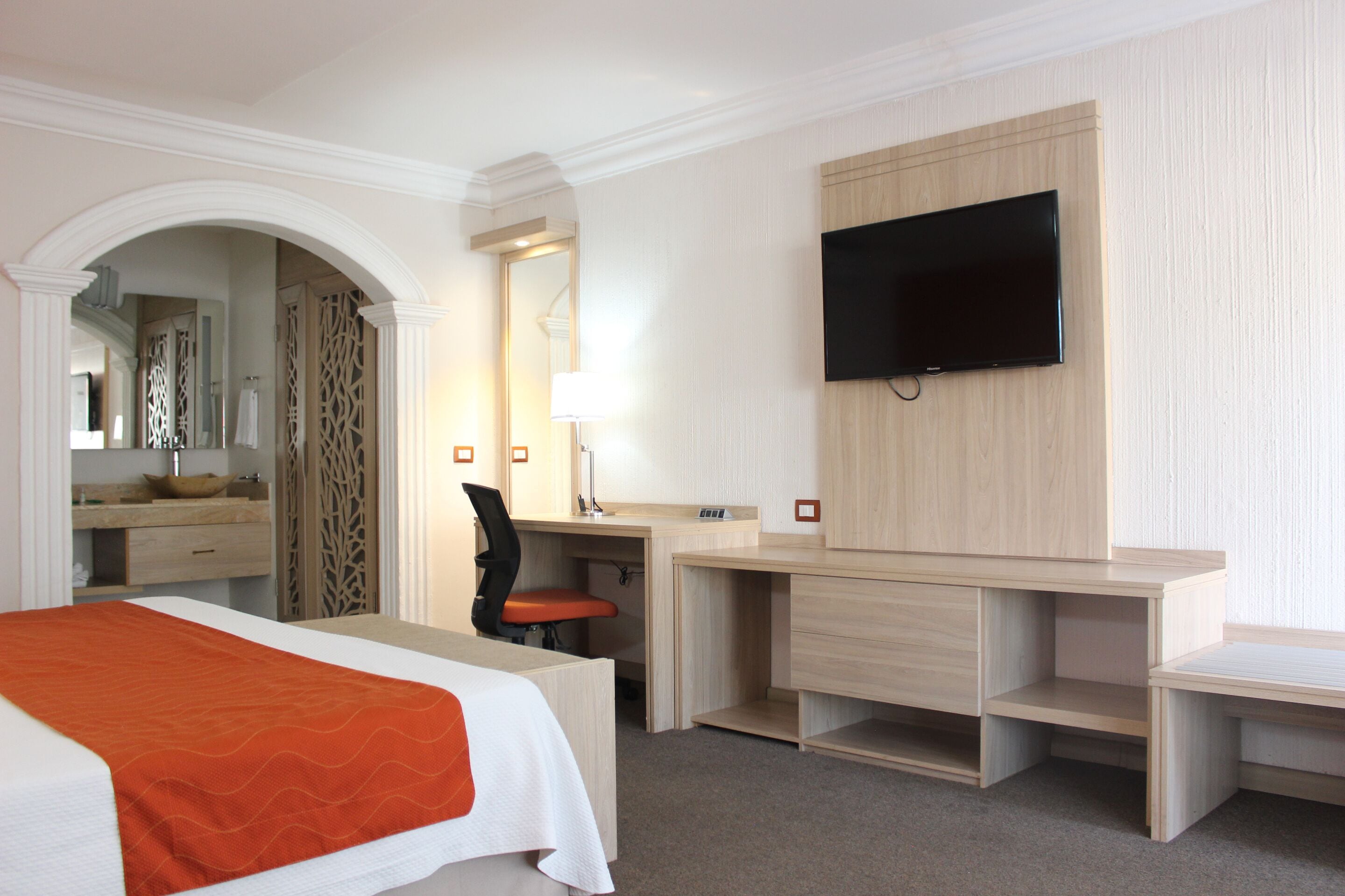 A hotel room with a bed, desk, chair, and a TV mounted on the wall.