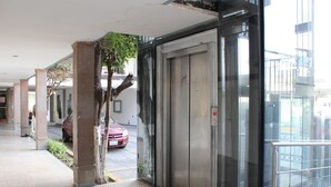 A corridor with a glass elevator, a red car parked outside, and a tree near the entrance.