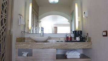 Une salle de bain avec un grand miroir, un lavabo, une machine à café et un porte-serviettes.