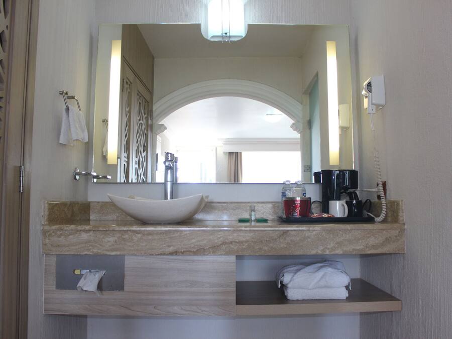 Une salle de bain avec un grand miroir, un lavabo, une machine à café et un porte-serviettes.