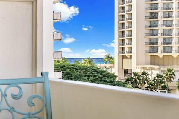 A balcony with a view of a high-rise building, palm trees, and the ocean.
