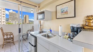 Un balcón con vistas a edificios altos, una cocina con microondas, fregadero y cafetera, y un cuadro en la pared.