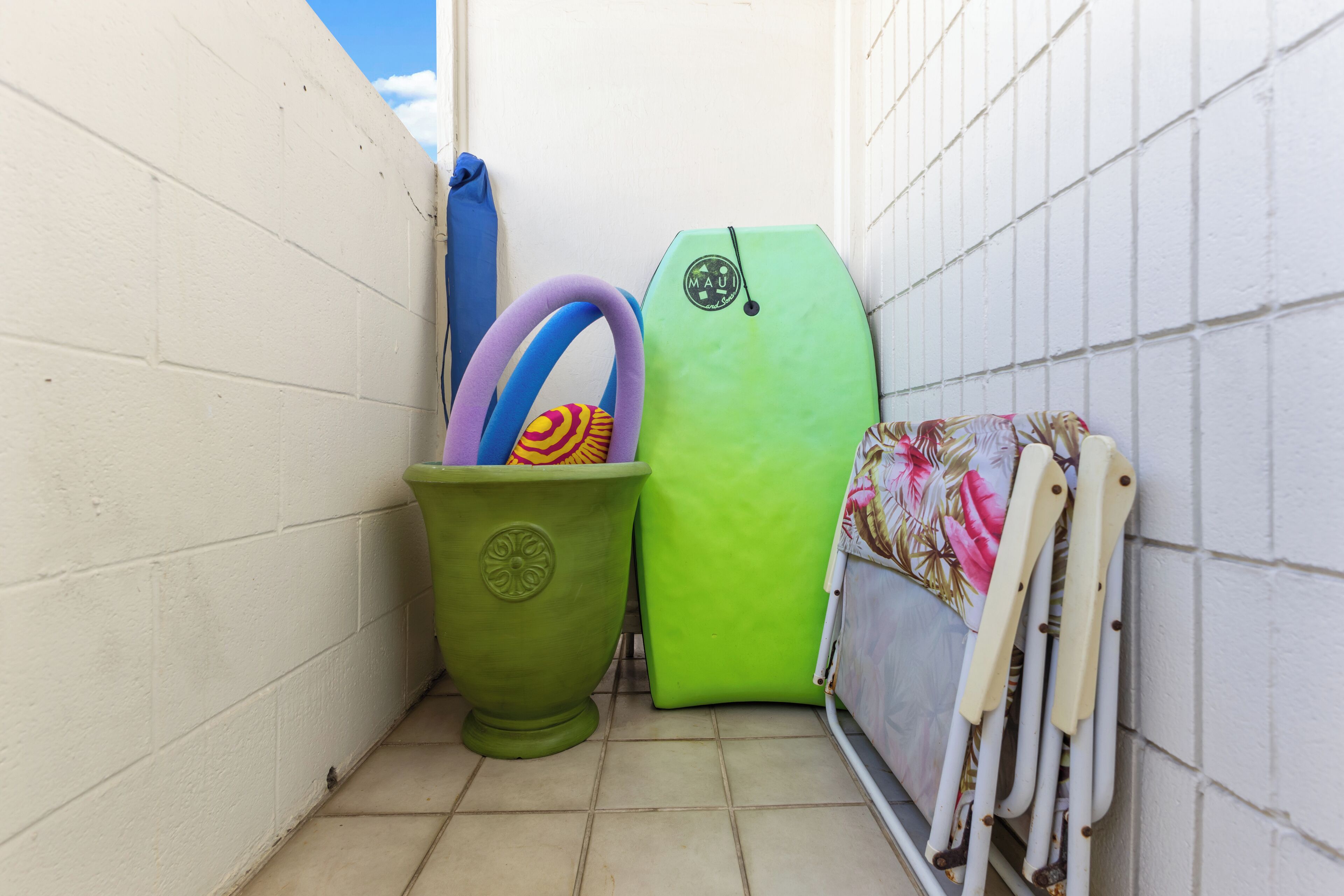 Kapea tila, jossa on valkoinen seinä, vihreä roskakori ja vihreä surffilauta nojaamassa seinään.