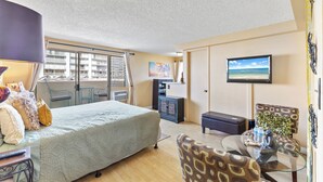 Habitación de hotel con cama, escritorio con lámpara, televisor en la pared y balcón con vistas a edificios.