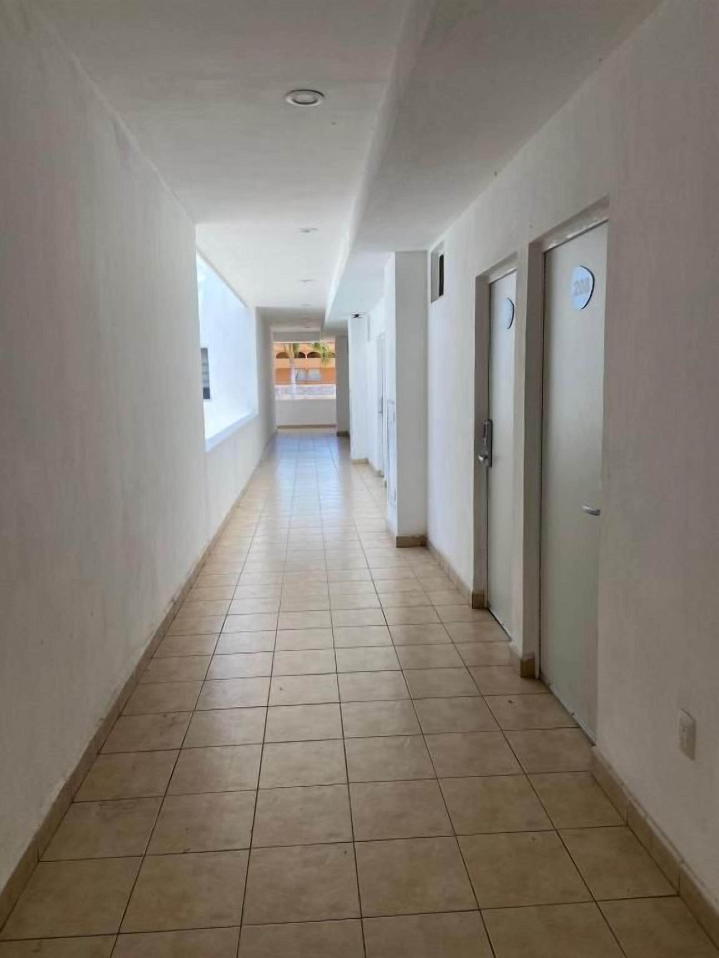 Un pasillo con puertas a la derecha, suelo de baldosas y una ventana a la izquierda.
