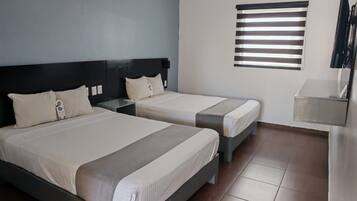 Habitación de hotel con dos camas, una mesita de noche, un televisor y una ventana con persianas.
