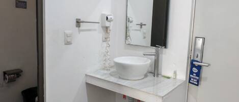 Un baño con lavamanos blanco, espejo y puerta con un cartel.